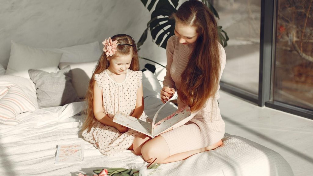 picture of mom and daughter reading book on bed