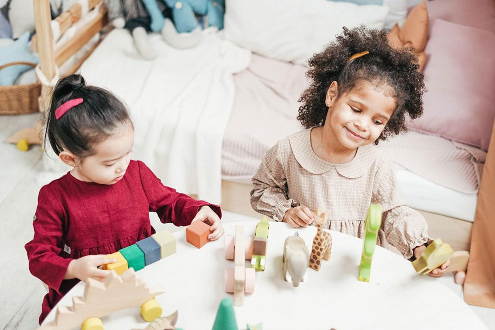 Picture of two kids sitting at a table playing with blocks and toys smiling